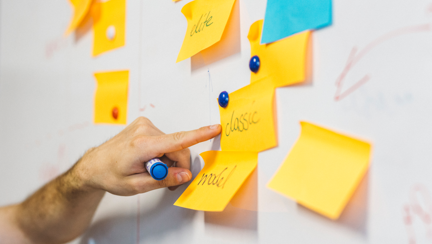 Hand pointing at sticky notes on a white board