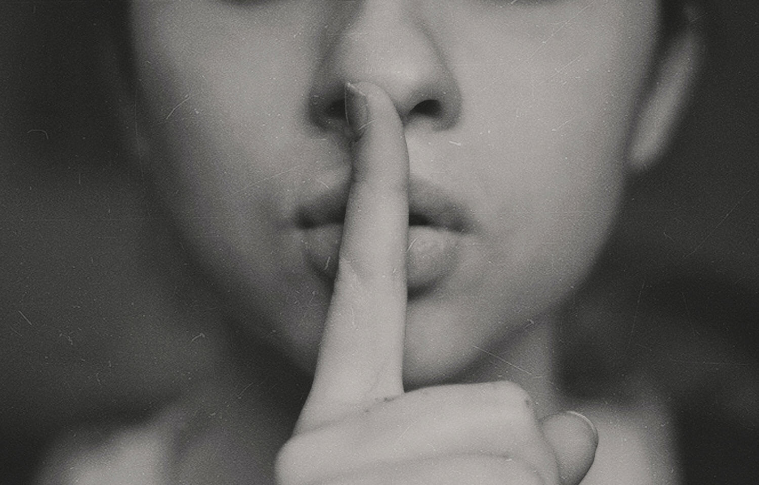 Photo of a person holding one finger to their mouth, as if to shush or to quiet someone.
