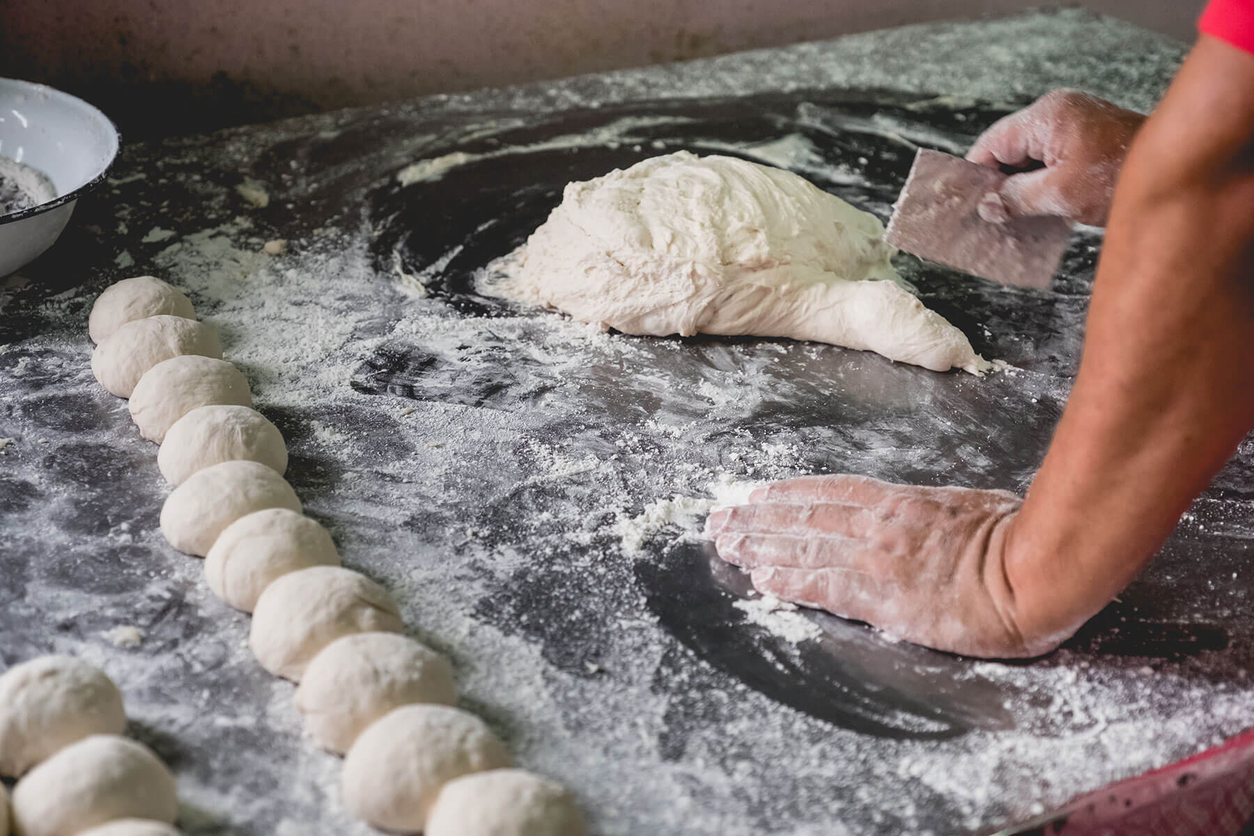 Two hands, covered in flour, shape a lump of dough into balls, ready to be formed into flatbread.