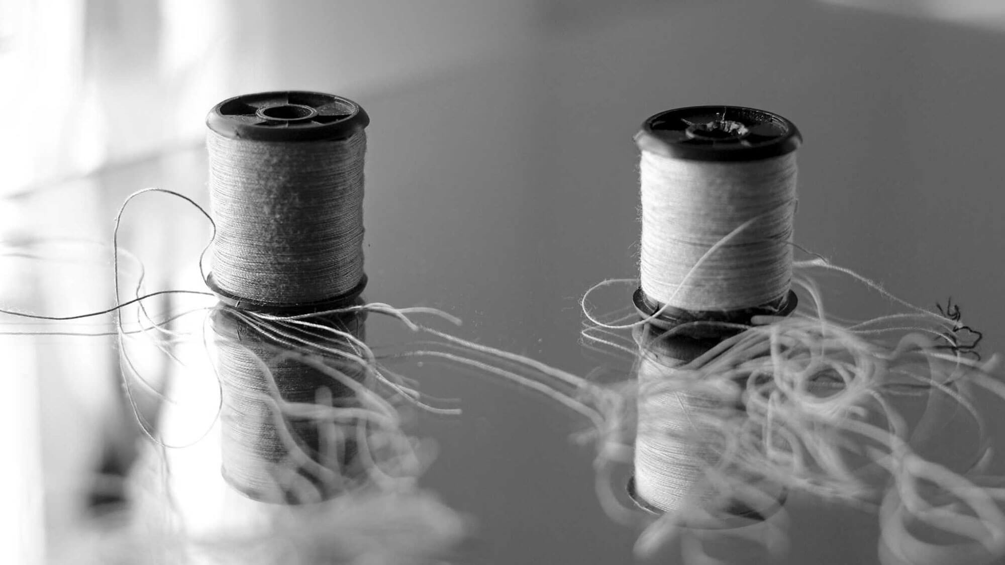 A black and white photo of two spools of thread — the threads are loose and tangled.