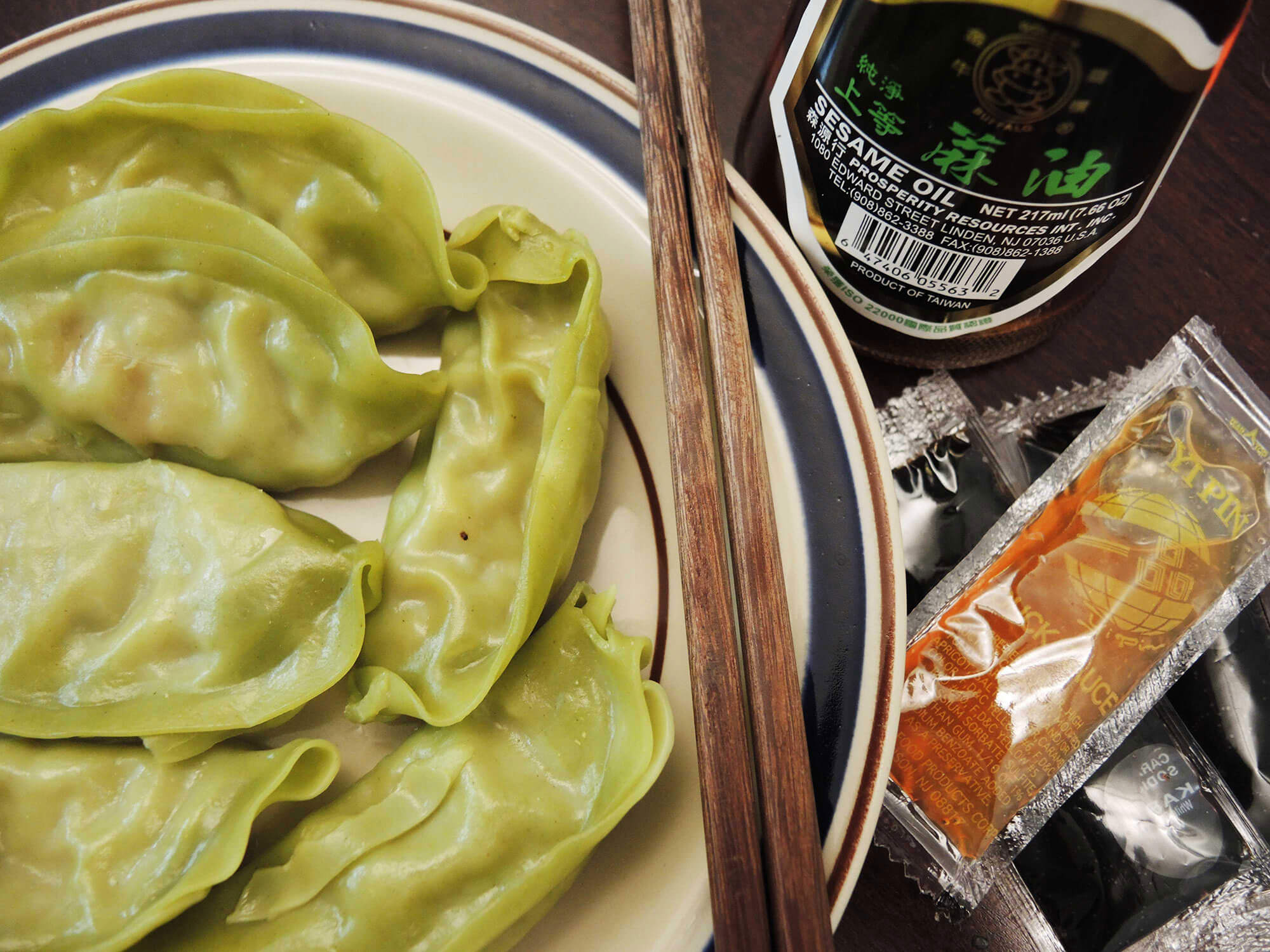 A plate of dumplings is accompanied by a bottle of sesame oil and packets of duck sauce and soy sauce.