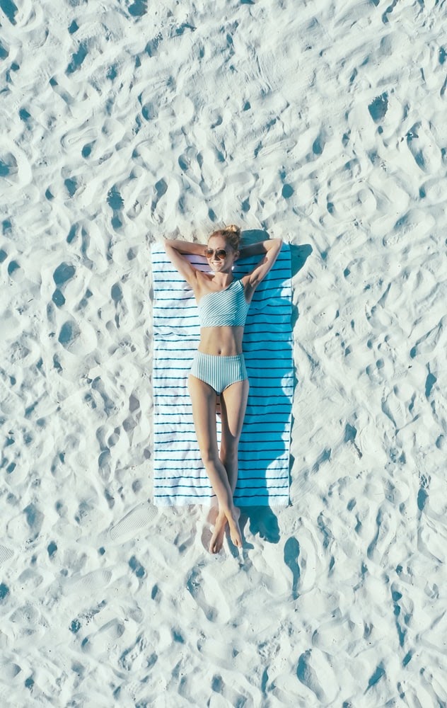 A woman enjoying a sunny day at the beach lying on a beach blanket