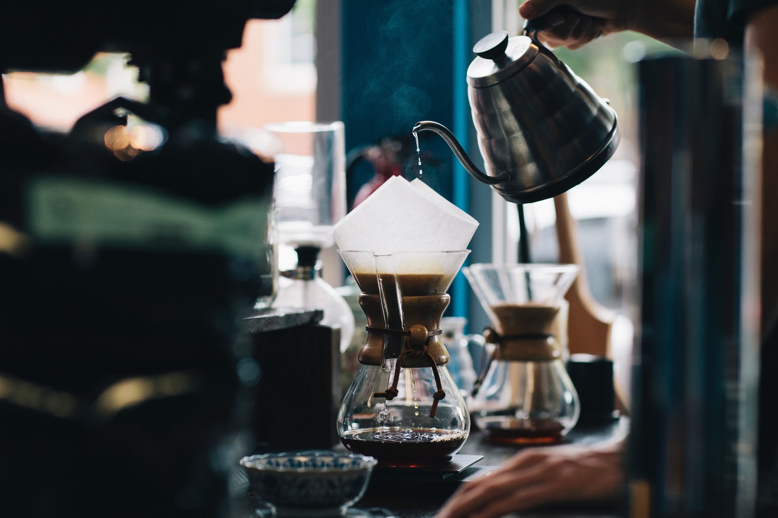 A person pouring water into a glass container brewing some coffee