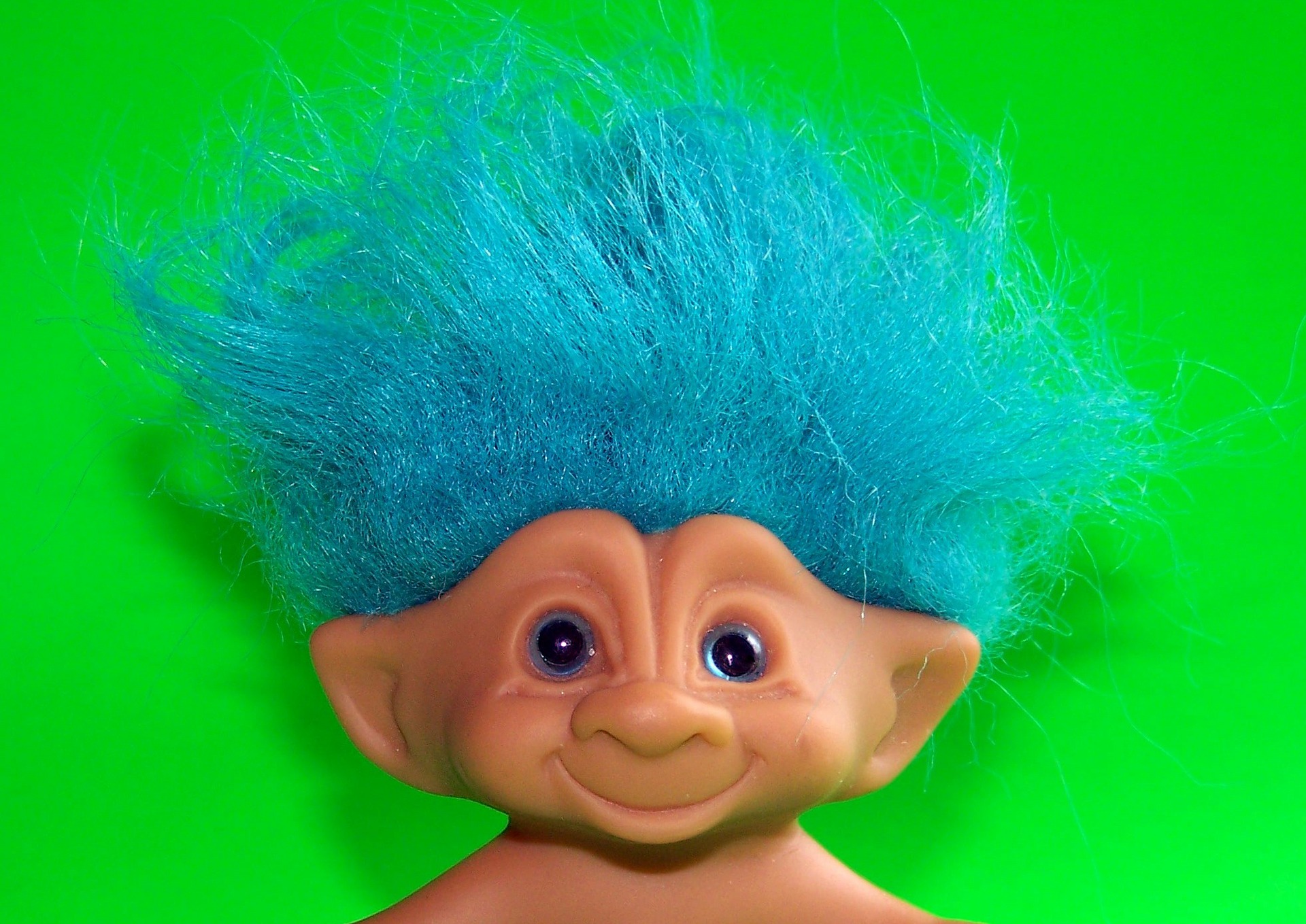A closeup of a smiling, blue-haired troll head in front of a neon green background.