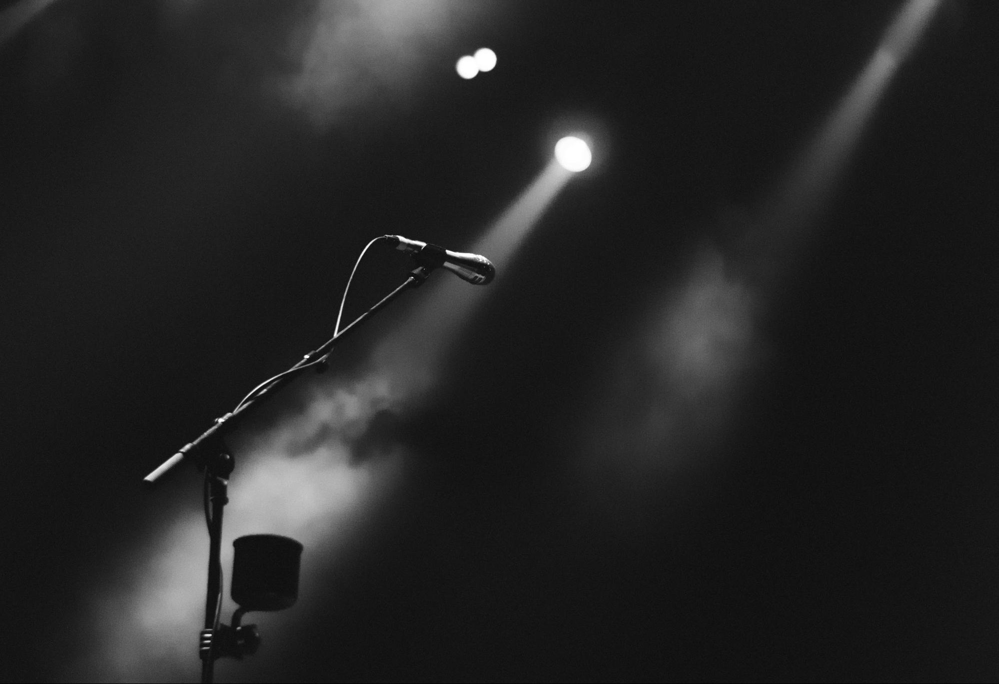 2 spotlight shining on a microphone in its stand on an empty stage.