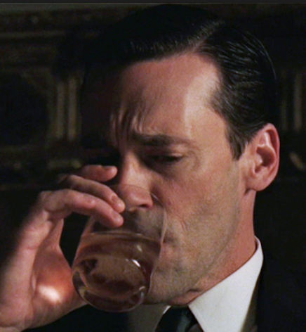 Don Draper drinking alcohol from a glass with a frown on his face.