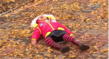 A toddler having a temper tantrum on a driveway covered in fallen leaves.