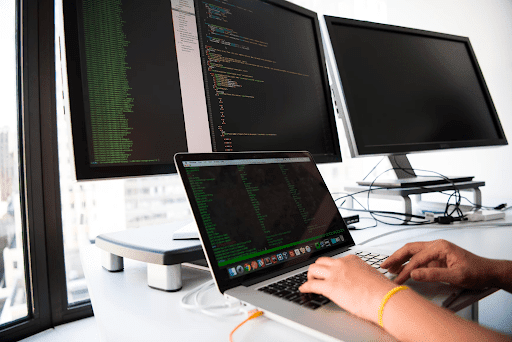 a person coding on laptop using extended monitors