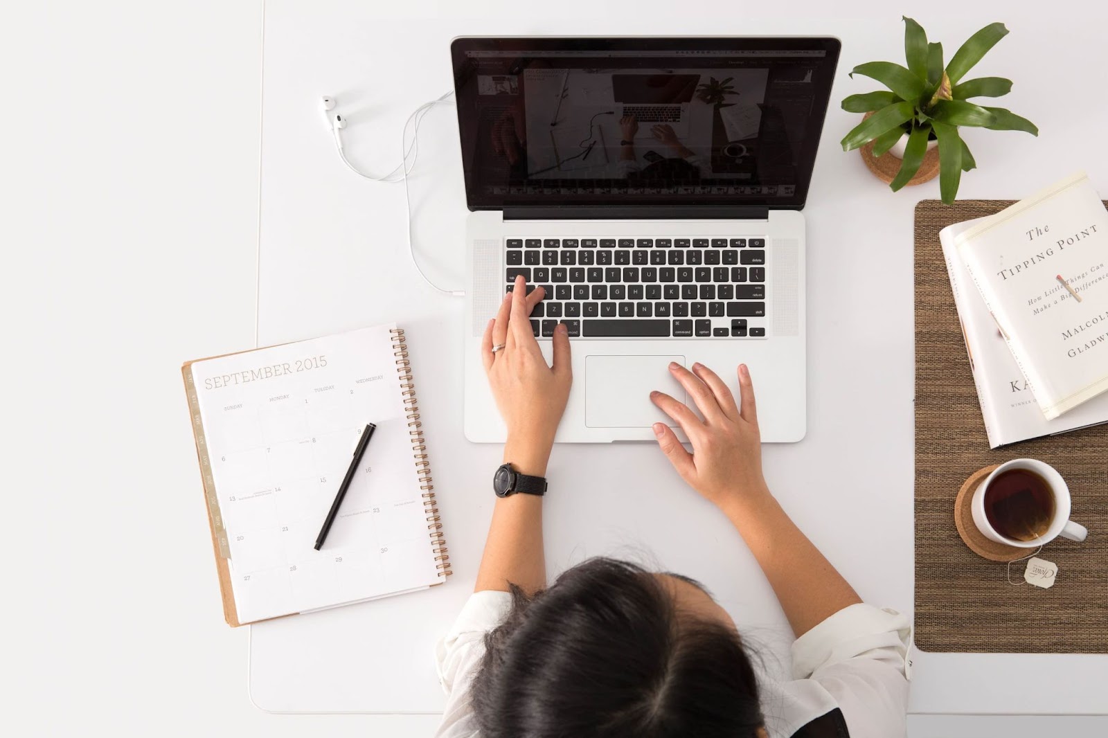 A woman using her laptop with planner and coffee at the table