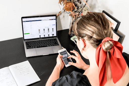 A woman working on a desk using her smartphone and laptop