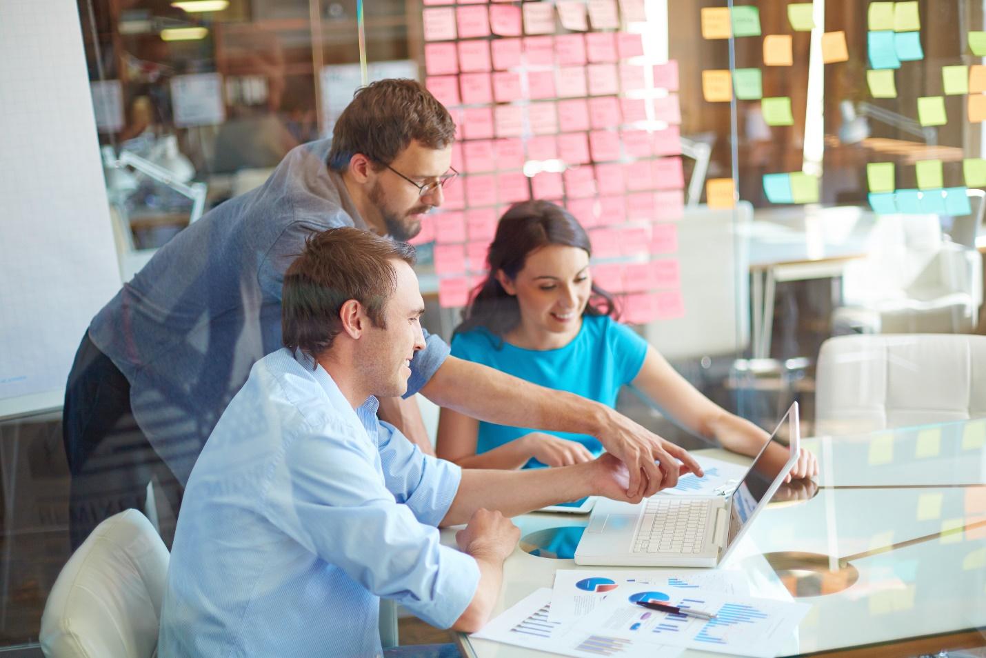 office team communicates via laptop, charts, sticky notes, and more on a group project