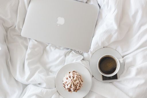 laptop, coffee cup, and a pastry on a bed