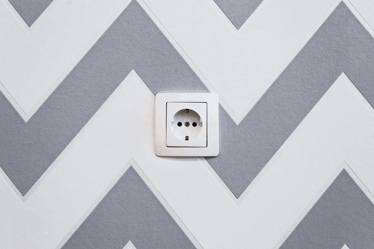 An electricity socket set against a grey and white wall.