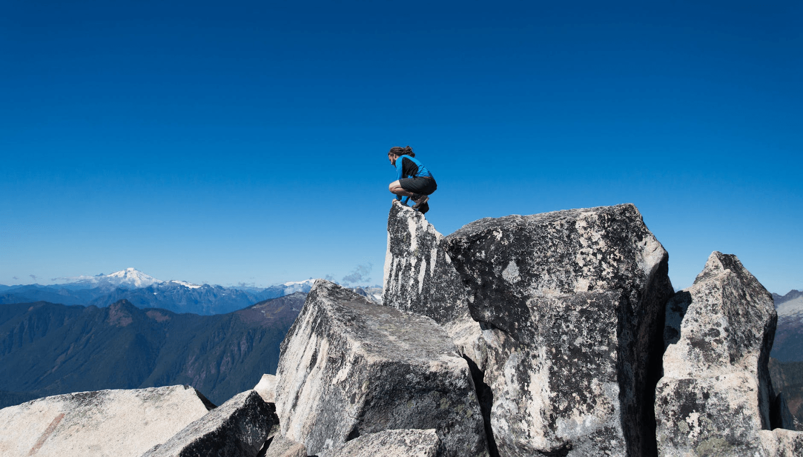 A man shown crouching at the top of a mountain.