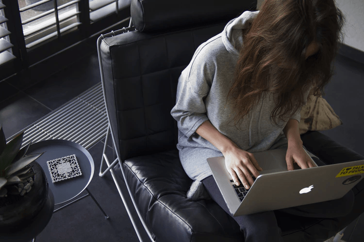 Woman sitting in a black leather chair and working on an Apple computer.