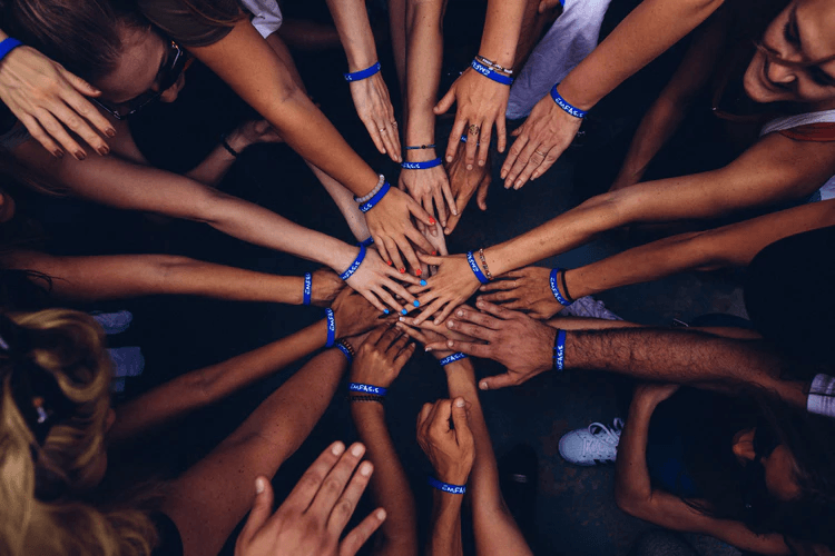 Many different people putting their hands into a circle.