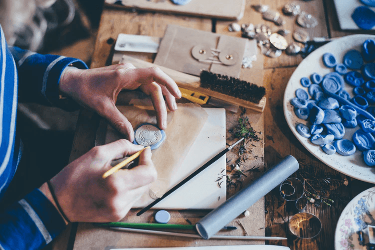A person doing hand crafts at a wooden table.