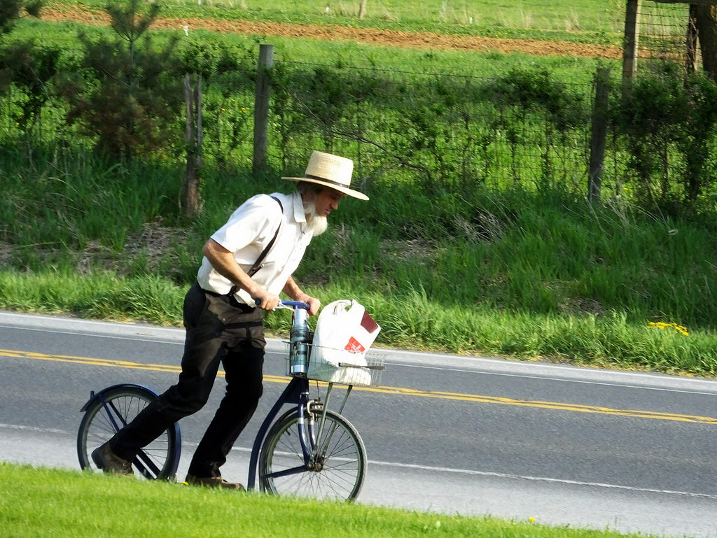 an amish man rides a bicycle next to a street in amish country ohio