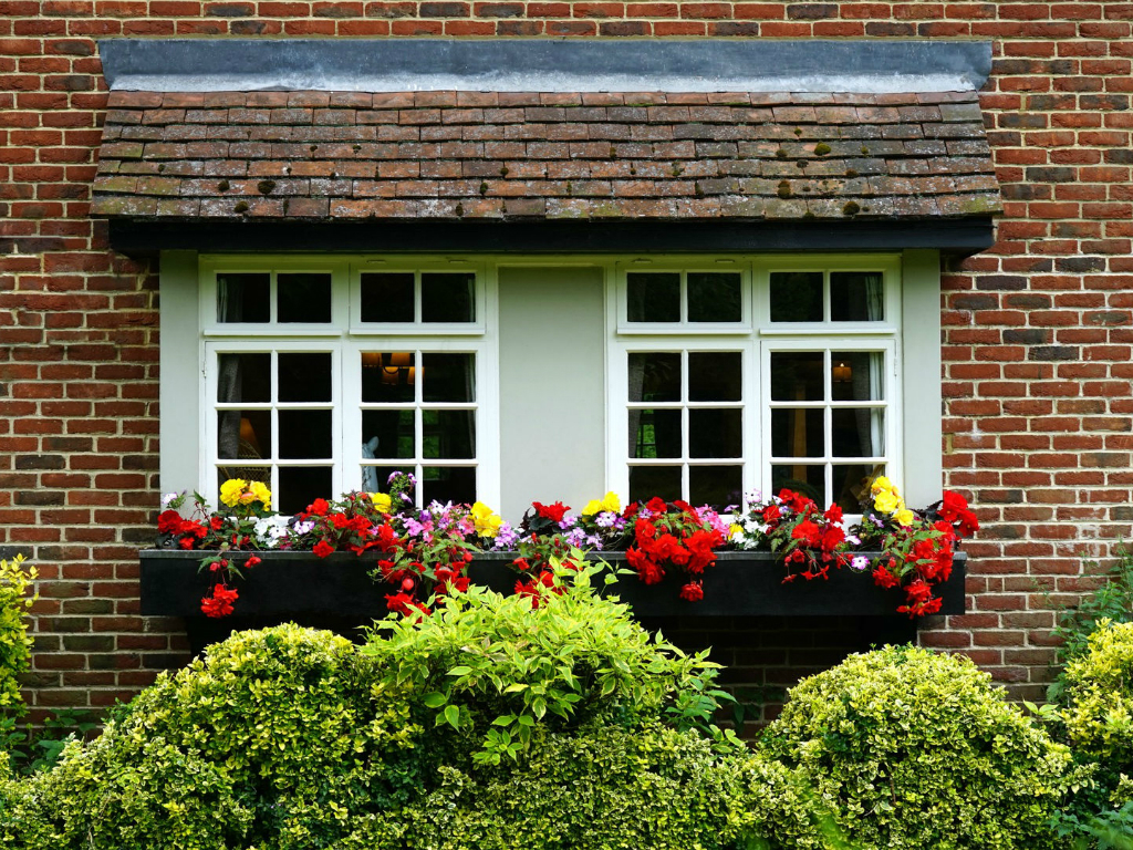 a red brick home with white windows and red flowers in window boxes