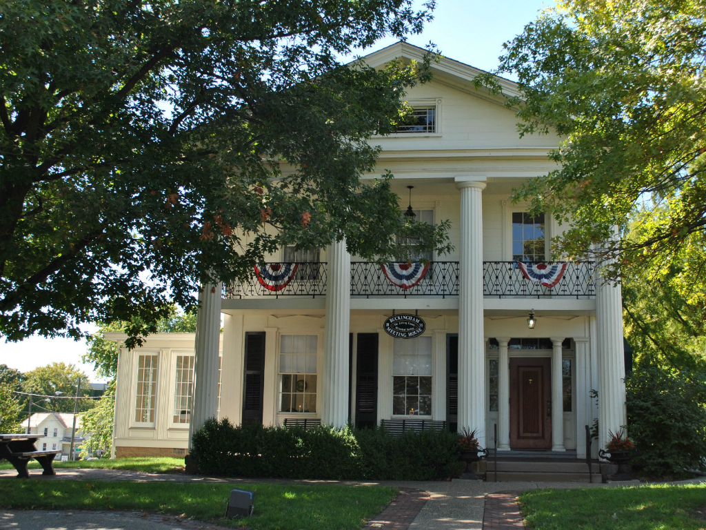 a white home in newark, ohio with columns half hidden by trees in the summer