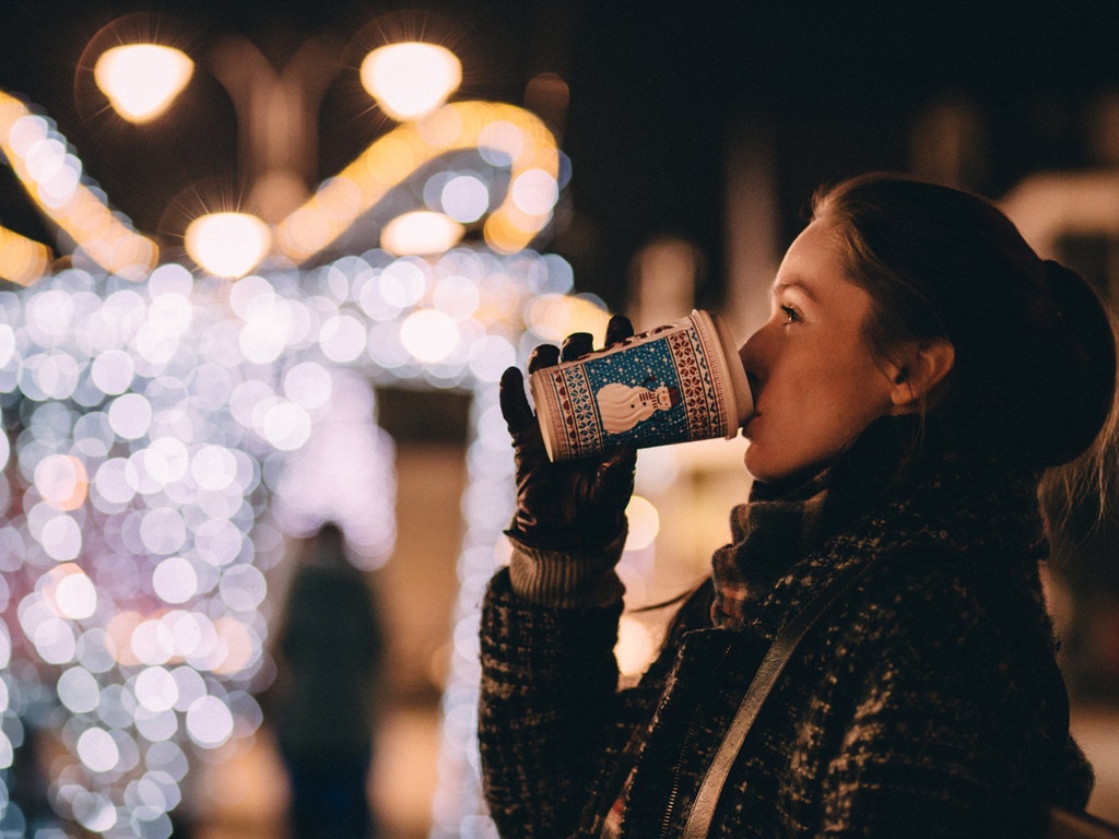 a woman drinking hot coffee during a holiday lights festival