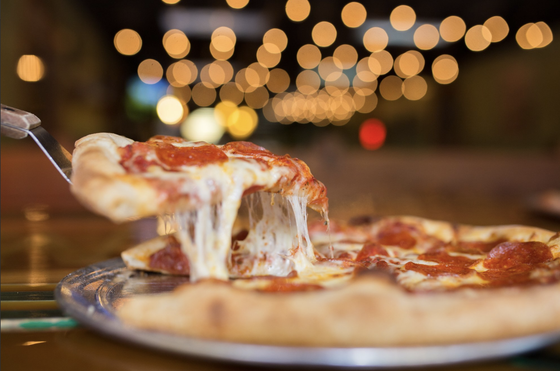 Cheesy slice of pizza being cut out of a pie