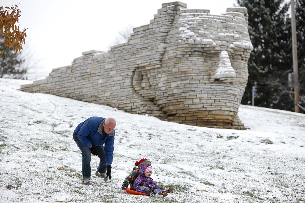 little girls sledding in snow next to brick statue in Dublin Park OH