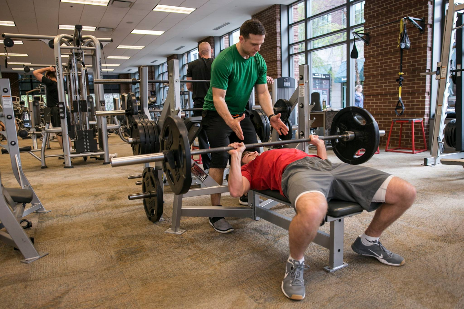 Man bench pressing with spotter at Arena Athletics,