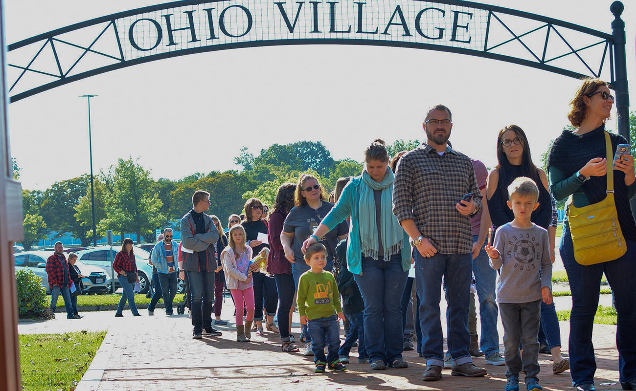 People waiting in a line under a sign that reads "Ohio Village"