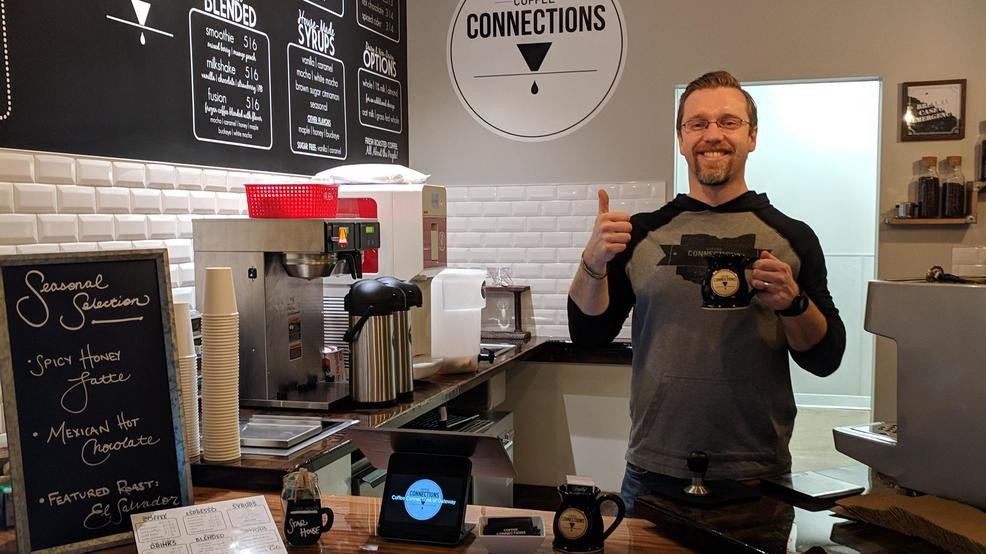 The owner of Coffee Connections in his first cafe in Hilliard, holding a mug of coffee and giving a thumbs up