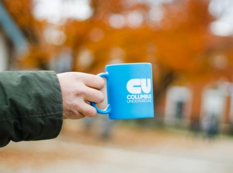 A hand holding out a free blue Columbus CoffeeFest mug