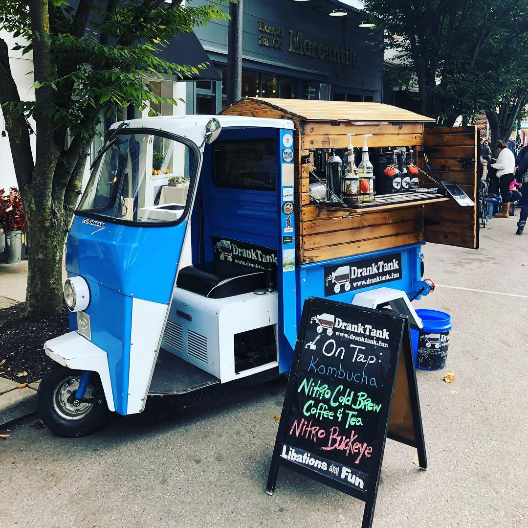 A moped with a rustic wooden coffee vending station attached to the back