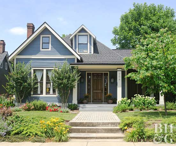 Blue two-story home with white trim and black and brown accents, lush greenery in front yard