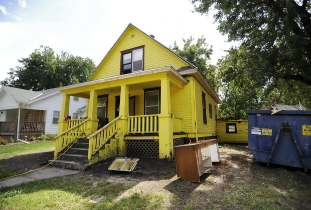 Dirty yellow two-story home with trash and dumpster