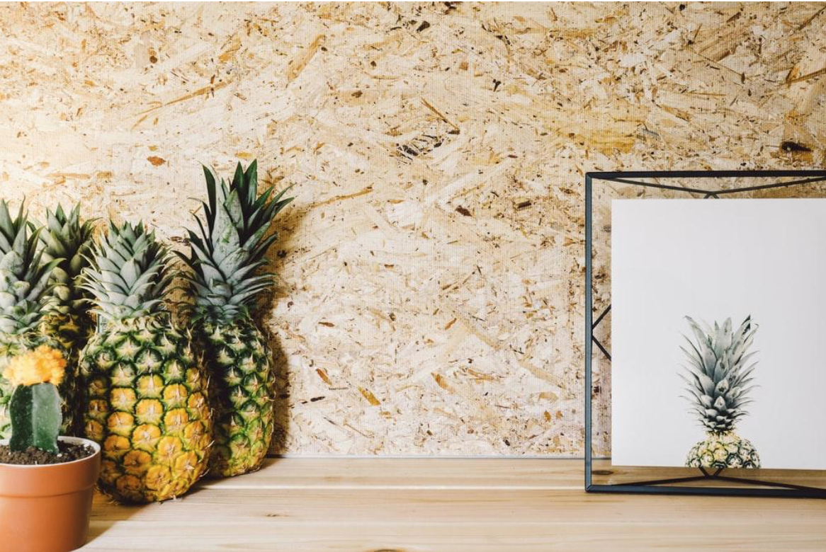 A holographof a pinball sits on a wood ledge next to a few pineapples and other textural elements.