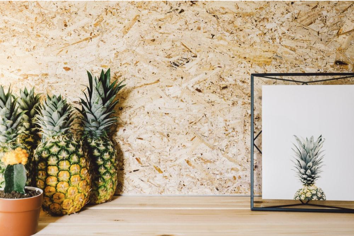 A holographof a pinball sits on a wood ledge next to a few pineapples and other textural elements. 