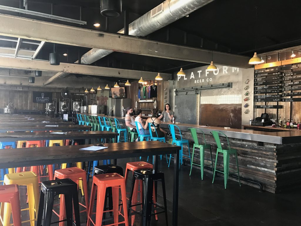 Three young adults sit at bar in Platform Beer taproom as bartender takes orders