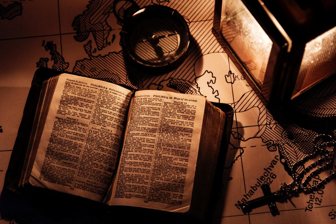 an old book open on a map beside a compass, a rosary, and a lantern