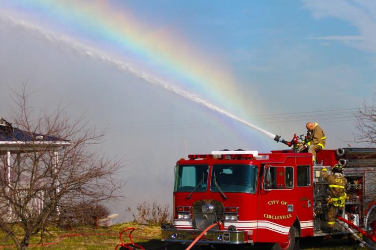 Firefighters put out a fire with a rainbow in the background