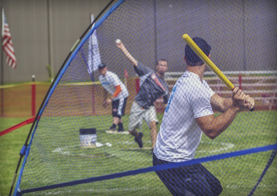 Pitching the ball to a man on home plate who has a yellow bat