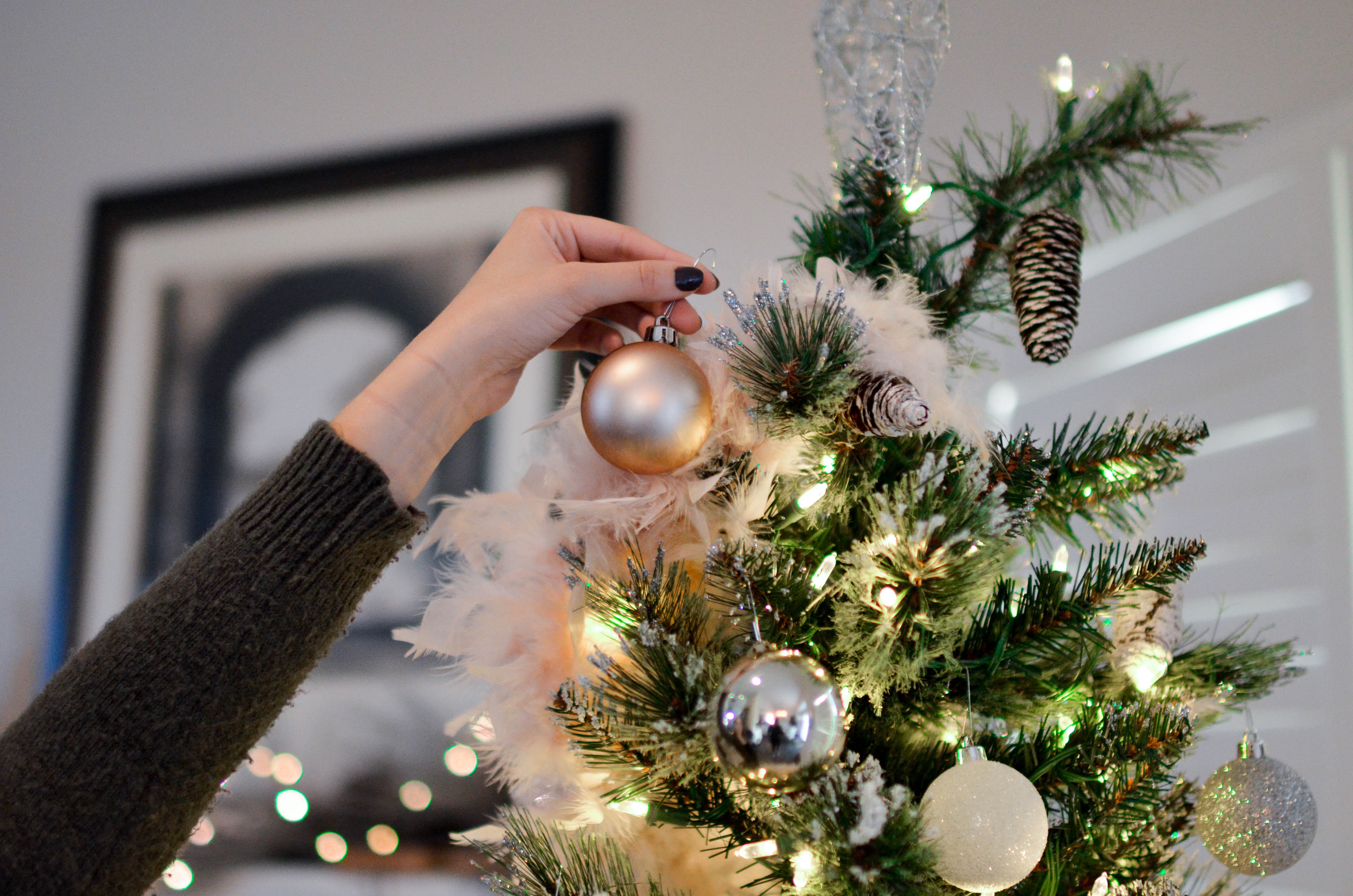 Hanfing a golden ornament on a tree with pinecones and christmas lights