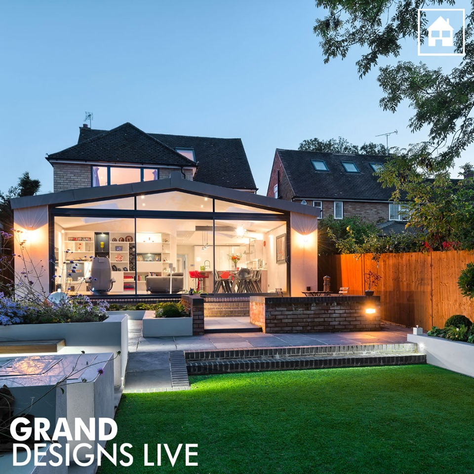 A backyard facing a home with a large bay window taking up most of the side of the house