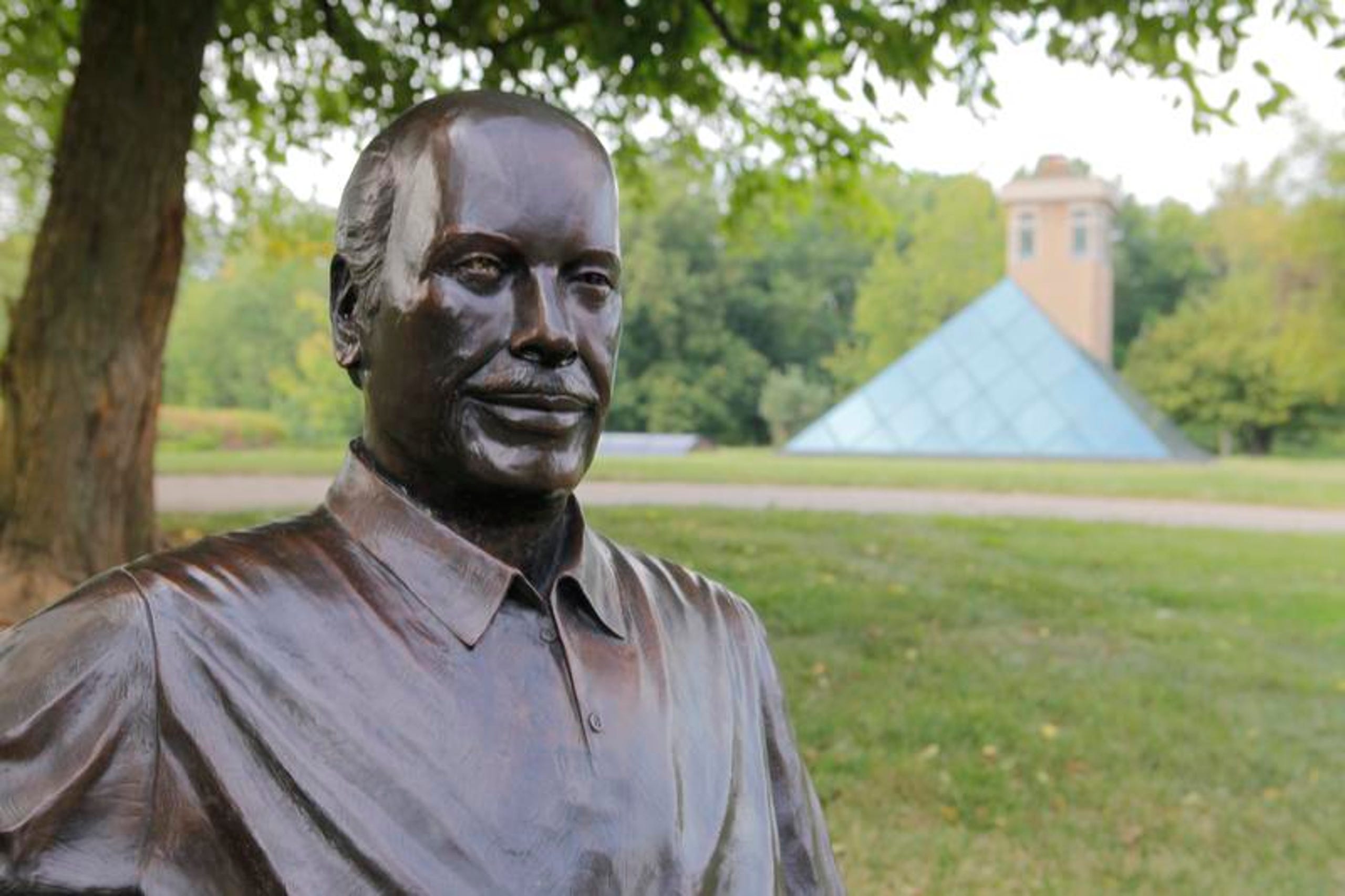 A statue of a man in the foreground, and in the back is the Pyramid House. Lots of green grass and trees in Ohio.