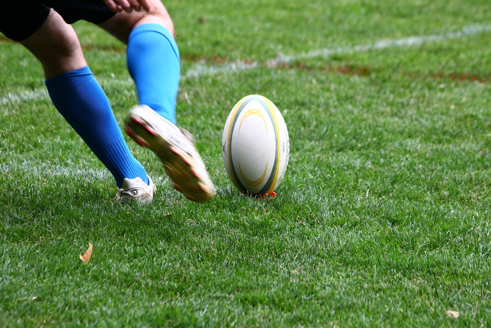 Man kicking a rugby ball on a brightly lit outdoor field where pest control services assess the risk of pest infestations