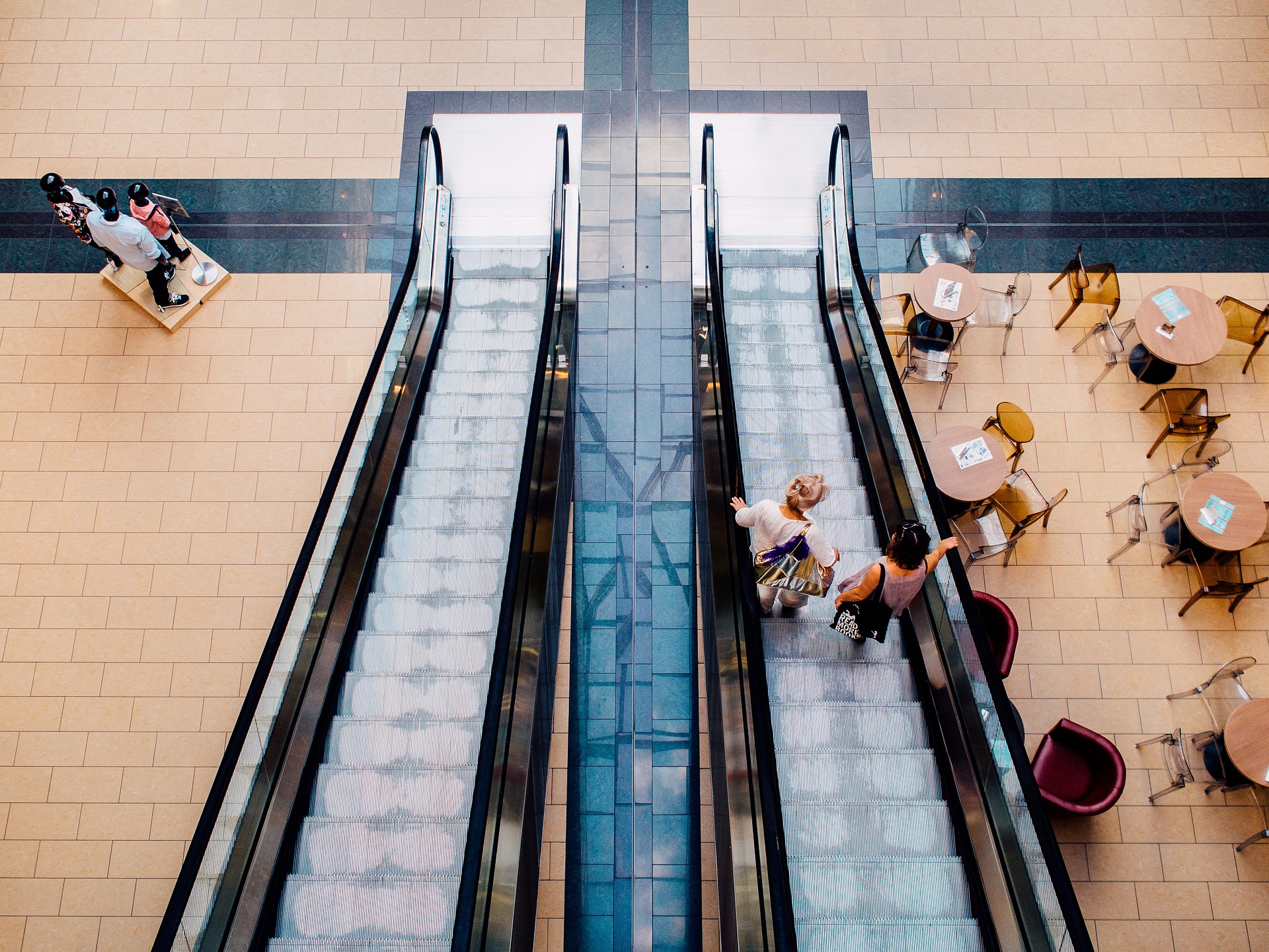 Two women stand on an elevator with cafe tables to one side and store mannequins on the other where Integrated Pest Management works best for shopping centre pest control