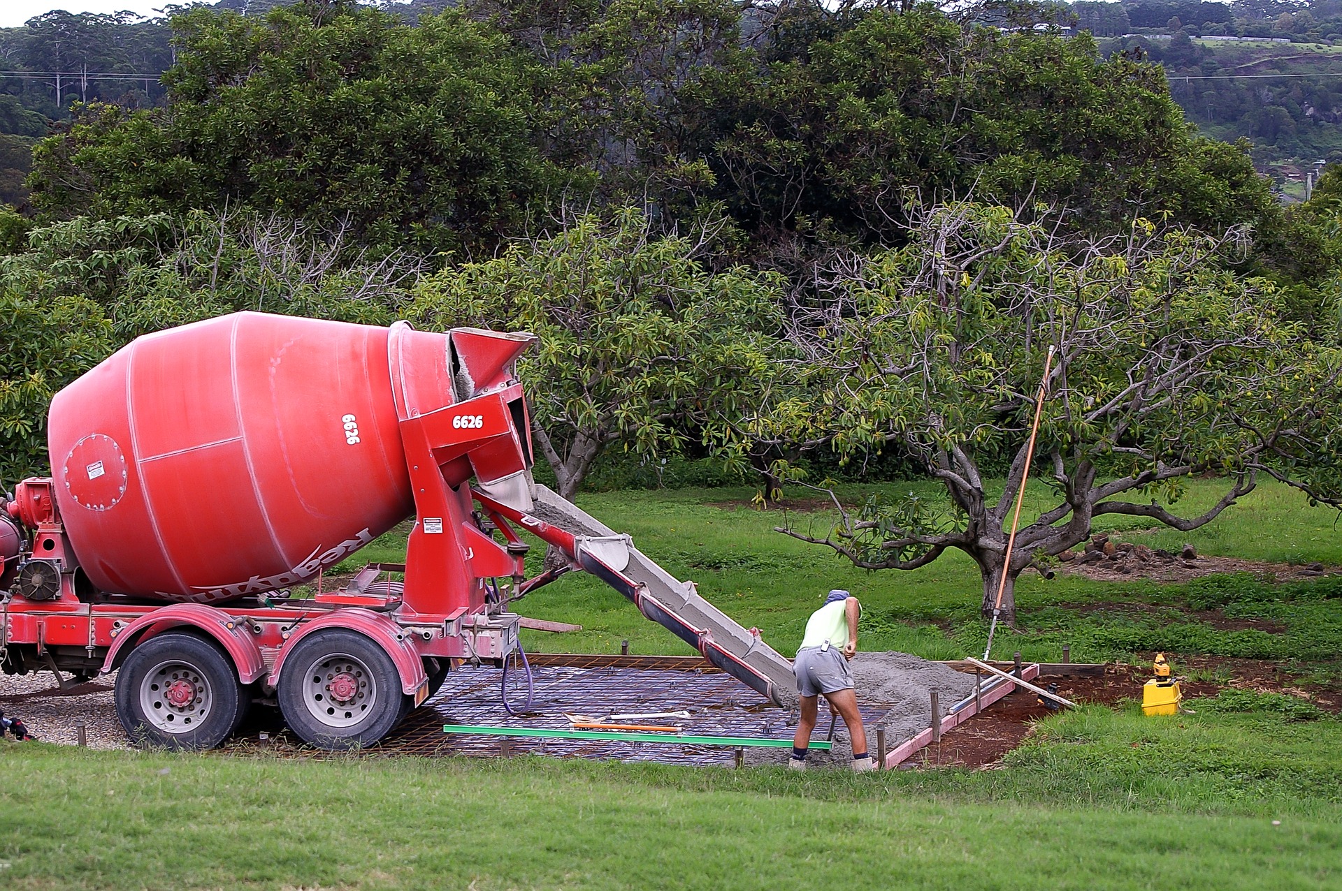 A red cement truck pours concrete with worker spreading the mix after the design and commencement of a termite protection systems.