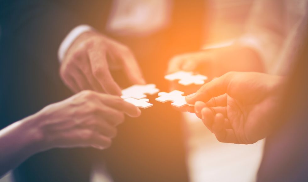 close up view of people holding jigsaw pieces to connect them together