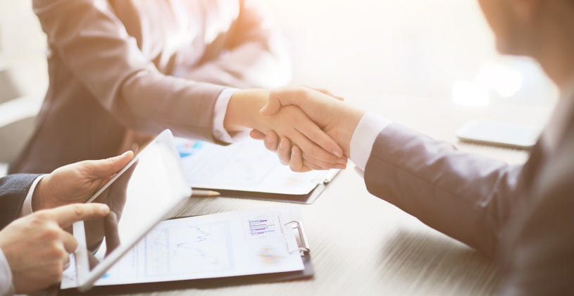 two people shaking hands whilst sitting at a desk