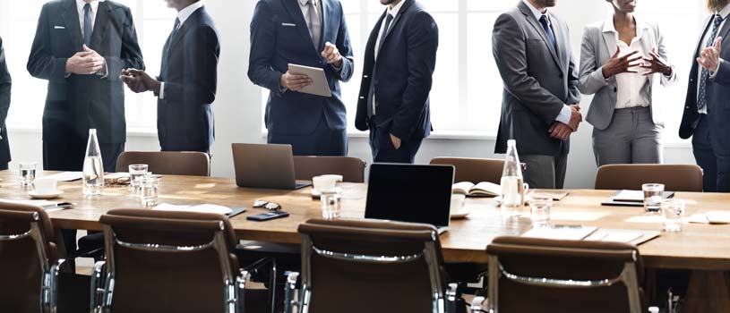 office workers in a meeting standing up in front of a long table