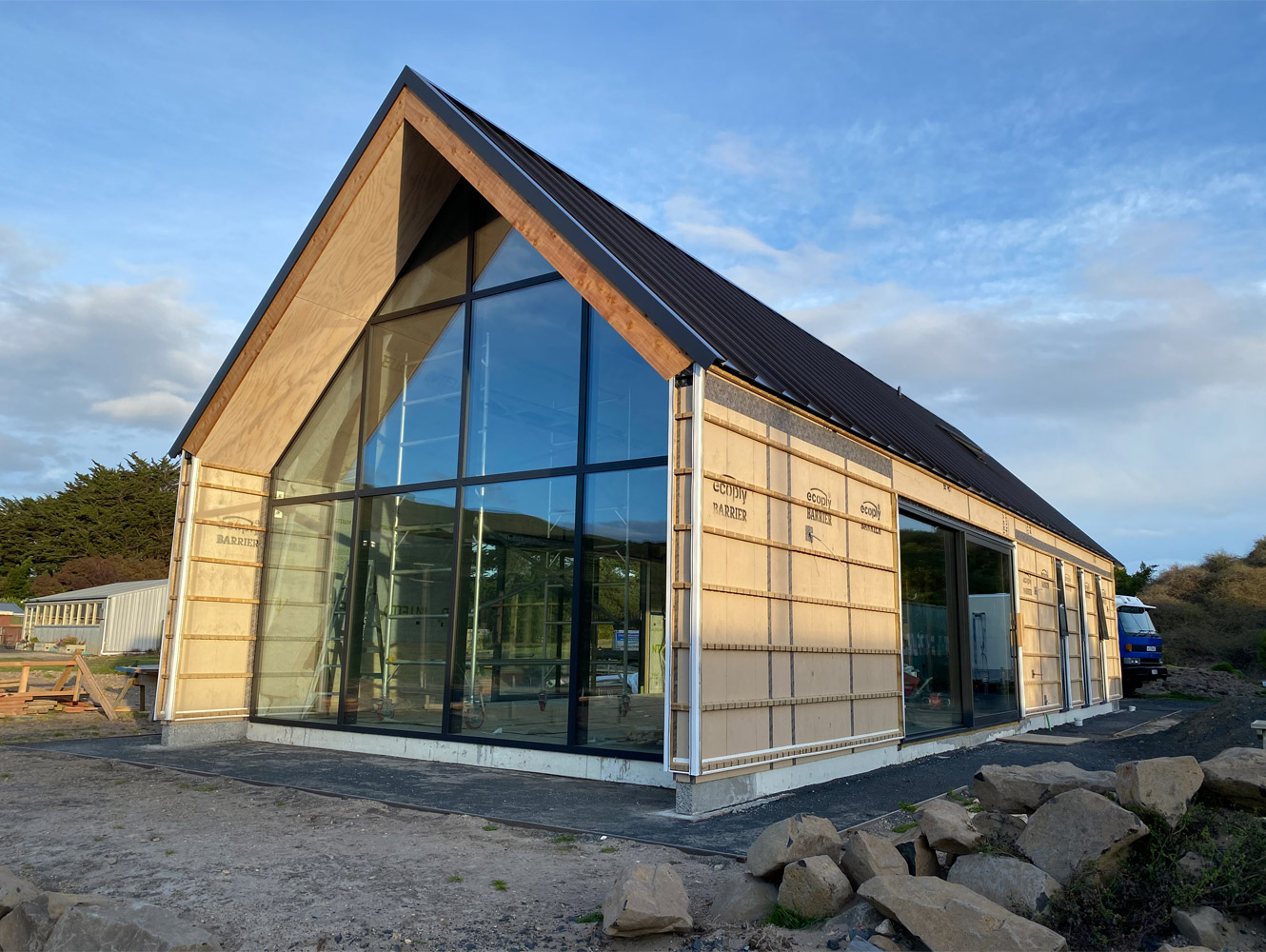 A photo of a house in the process of being built with a gabled roof and a big glass window at the front